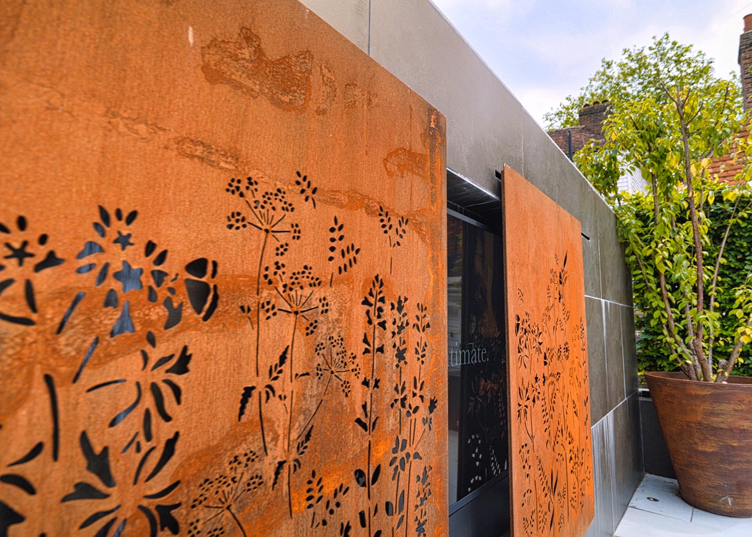 Outdoor metal panels with cutout floral patterns beside a planter