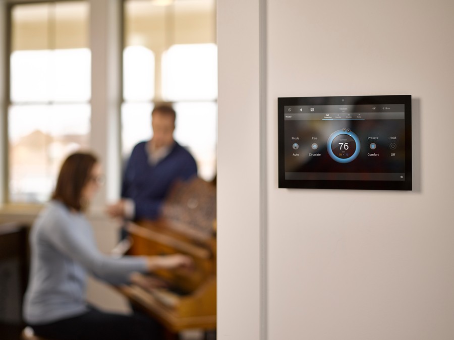 A Control4 system tablet interface on a wall in a Park City home, with a couple blurred in the background.