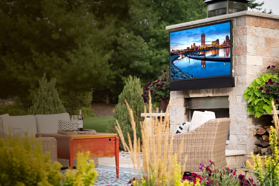 An outdoor TV is mounted on a stone fireplace on an uncovered patio in the backyard of a Park City home.