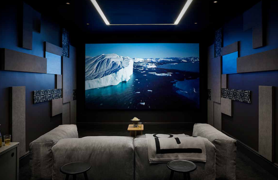 A modern home theater with in-wall speakers, a couch, and a large screen.