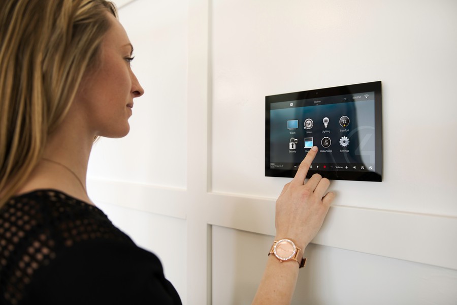 A woman controls a smart home through a wall-mounted touchscreen.