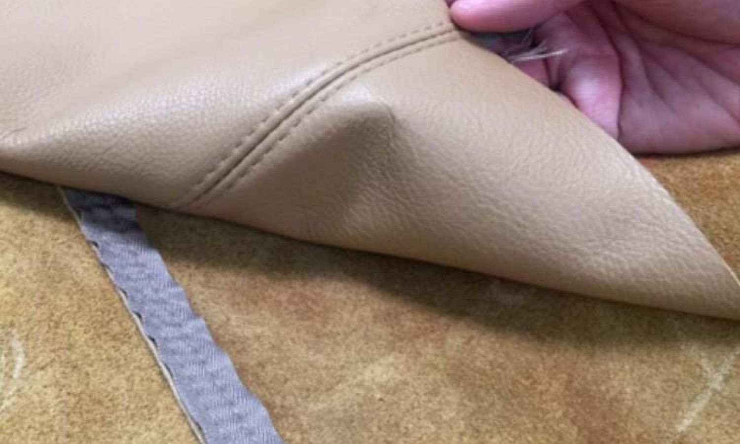 a hand pulling back fine leather with stitching visible
